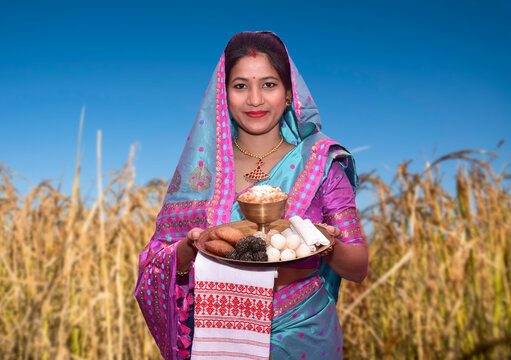 Woman wearing traditional costume holding a tray full of Magh Bihu traditional food.