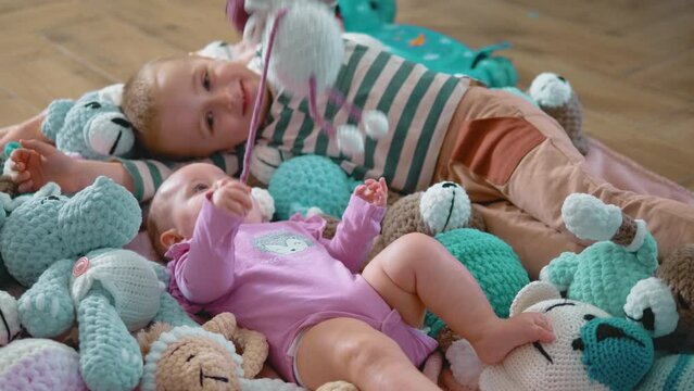 Happy baby at the age of three months lies among stuffed toys and plays with his older brother