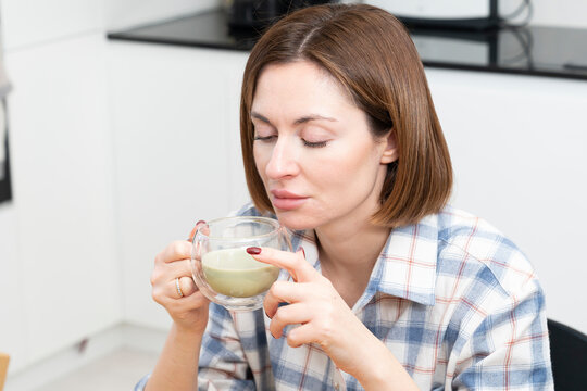 Close-up portrait of attractive girl drinking hot matcha tea in the kitchen