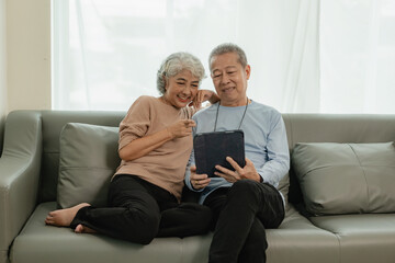 Asian senior couple looking at camera and smiling, senior smiling and looking at tablet Retired...