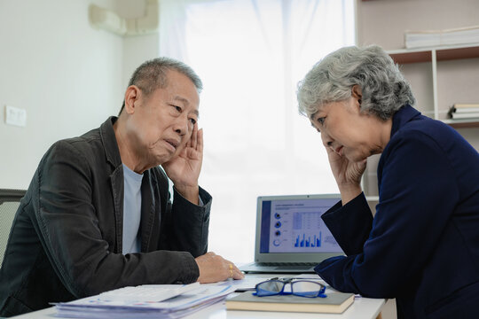 Two senior Asian businessmen, male and female, are stressed out with paperwork and are tired, have headaches and office syndrome from working hard with financial documents at the desk in the office.