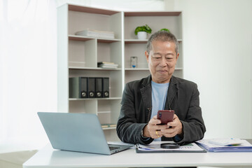 Naklejka premium Senior Asian businessman uses smartphone to talk with customers Work on your laptop and discuss with clients about the requirements of a modern office or co-working space, startup.