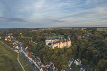 A majestic castle sits nestled among a lush forest of green trees in an aerial perspective, showcasing a harmonious blend of man-made architecture and natural surroundings