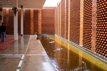Modern interior of semi outdoor mosque (masjid) with unique exposed red brick facade and pond on...