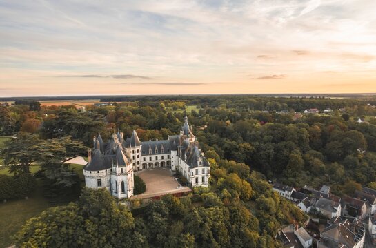 A stunning aerial view showcases a grand castle nestled within a sea of verdant trees, offering a captivating scene of history and nature merging seamlessly