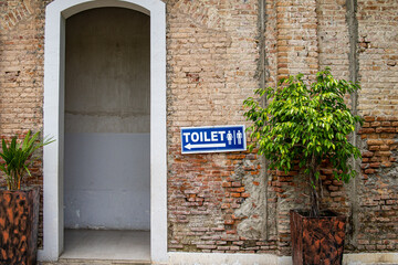 Toilet sign for men and women with arrow in white and blue attached to red bricks wall.