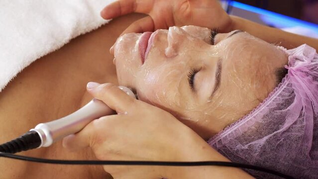 Woman in a spa salon on cosmetic procedures for facial care. Beautician makes medical procedures using a medical equipment. Cosmetologist making a woman a therapeutic procedure on a face.
