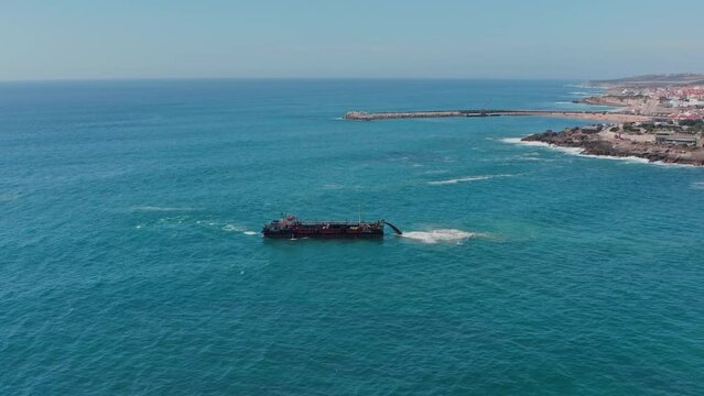 Aerial view to the working dredger ship in the ocean on sunny day. Dredger works in the sea.  A marine vessel washes sand. Sea ship deepens the coastal ocean floor near touristic Ericeira city.