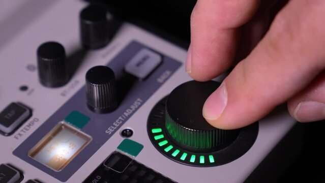 Close-up image of hand adjusting mixer knob for volume control during live studio performance. Mixer features multiple knobs and buttons for precise audio mix adjustments.