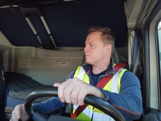 Truck Driver driving with high Visibility Vest and Red Seat Belt on, behind the Steering Wheel of a...