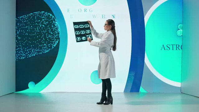 A woman in a white coat stands in front of a drug product on a large digital screen. A female scientist demonstrates a picture of the lungs and gives a scientific lecture.