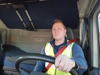 Truck Driver driving with high Visibility Vest and Red Seat Belt on, behind the Steering Wheel of a...