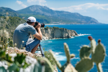 Male photographer with camera on tripod captures coastal seascape.