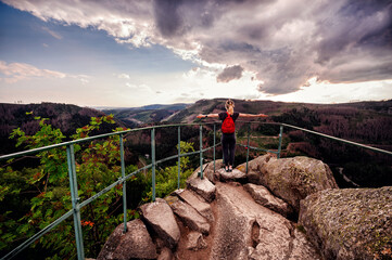 An adventurer with arms wide open embraces the grandeur of the wilderness from a rocky lookout point, under a dynamic sky