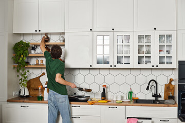 back view of man in casual dark green t shirt doing chores in kitchen during spring cleaning