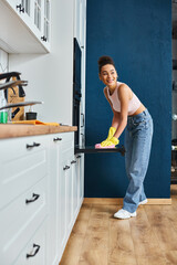 Fototapeta na wymiar cheerful beautiful african american woman in casual outfit washing oven in kitchen, spring cleaning