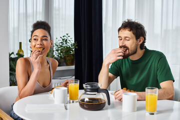 Fototapeta na wymiar beautiful jolly diverse couple in homewear enjoying their delicious breakfast while at home