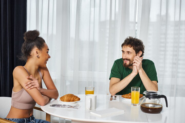 Obraz na płótnie Canvas appealing beautiful interracial couple in casual outfits enjoying their delicious breakfast at home