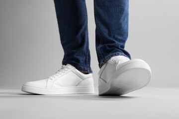 Man wearing stylish white sneakers on grey background, closeup