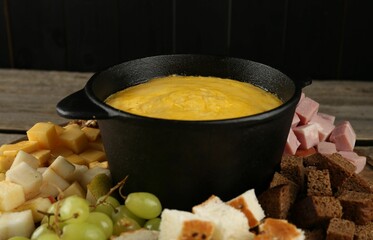 Fondue pot with melted cheese and different products on table, closeup