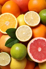 Different fresh citrus fruits and leaves as background, top view