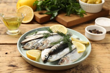 Fresh raw sprats, lemon and dill on wooden table, closeup