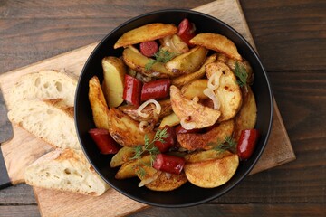 Delicious baked potato with thin dry smoked sausages in bowl and bread on wooden table, top view