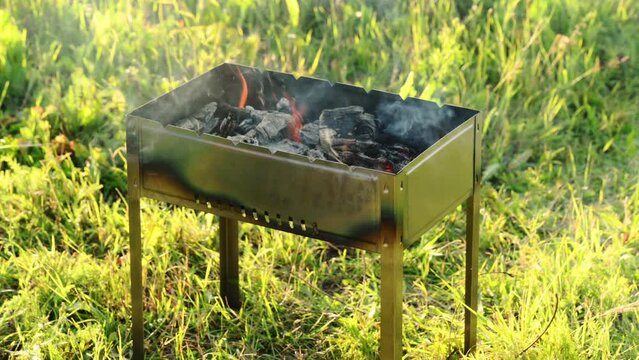 Metal brazier for a picnic and barbecue with burning wood, coals, flames on a summer sunny day in nature. Weekend holiday concept, cooking on coals.