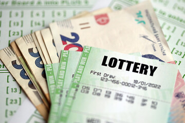 Green lottery tickets and ukrainian money bills on blank with numbers for playing lottery close up