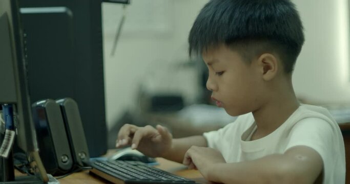 An Asian boy in elementary school is having fun using his desktop computer to play games and look at social media on a holiday at home.