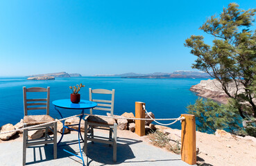 Greek gray chairs and blue table on a typical sunny terrace with a lovely view near the Lighthouse of Akrotiri, Santorini. Greek Islands, European Vacation. 