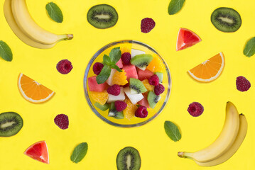 Fruit salad in the glass bowl, fruit and berry on the yellow background. Top view.