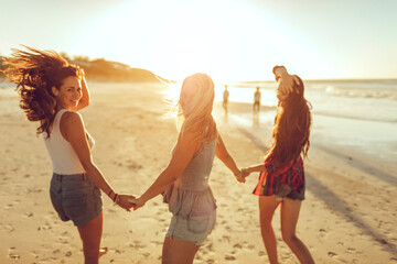 Happy women holding hands on the beach at sunset