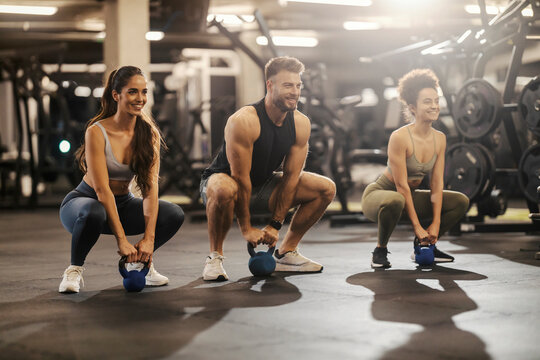 Fit friends in shape doing kettle bell squats in a gym.