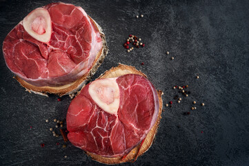 raw Ossobuco. Veal shanks Ossobuco with pepper, lemon and garlic for gremolata, typical ingredients of Italian Lombard cuisine, top view on dark background