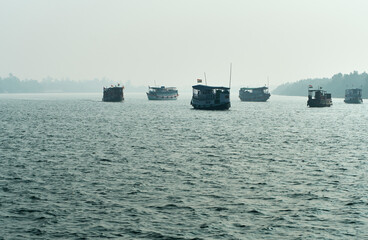Silhouette of traditional tourist vessels and fishing boats cruising through vast waterbody at Sundarbans biosphere reserve in a foggy winter morning. Sundarbans is a popular ecotourism destination.