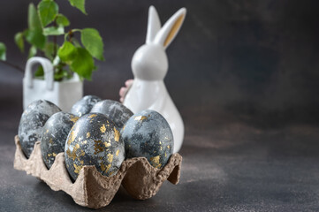 Spring Easter still life. White rabbit and eggs painted with gold pattern on a gray background.....