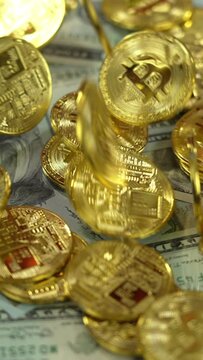A slow motion vertical view of dropping golden Bitcoins over rotating US currency.  	