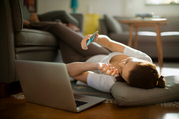 Smiling woman using smartphone on living room floor