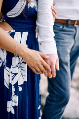 Woman stands, hugging man arm and touching his palm with her palm. Cropped. Faceless