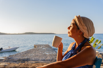 Beautiful woman intensely enjoying a morning coffee from a Greek tavern at sunrise with the Aegean Sea as a background