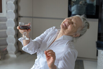 a woman of retirement age in a white blouse drinks wine by the fireplace