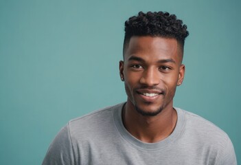 A stylish man with a trendy haircut smiling softly at the camera. He is wearing a grey shirt and has a friendly appearance. - obrazy, fototapety, plakaty