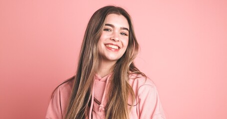 Smiling young woman on peach background looking at camera in studio