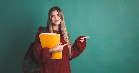 Happy female university student pointing to copy space and holding books