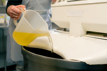 close up a baker woman adding sunflower oil from a measuring cup in a professional kitchen