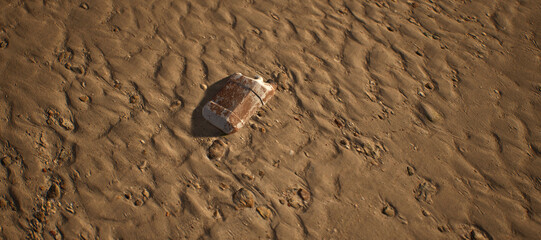 Dirty white plastic oil container lying in rippled sand of beach.