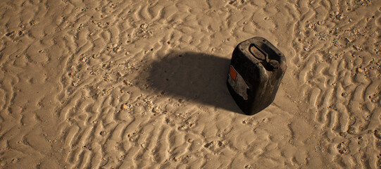 Plastic black container lying in rippled sand of beach. - 746726123