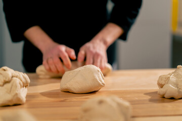 close up layout in a professional kitchen of bakers at the table process the dough and form it into...