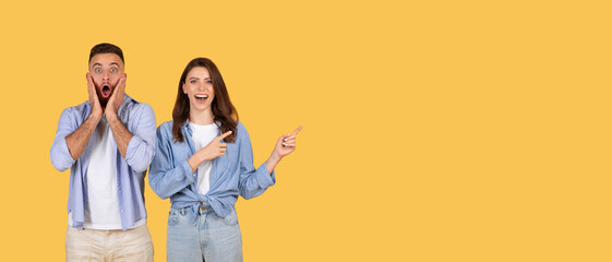 Amazed young man and excited woman pointing at free space on yellow, panorama